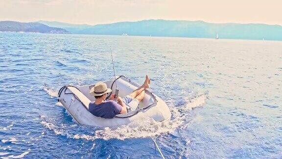 在阳光明媚的夏日海洋上年轻人在筏子上钓鱼和使用智能手机实时