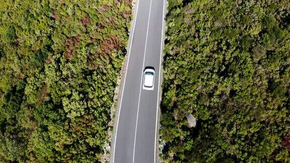 4K鸟瞰图白色家庭汽车行驶在绿色山丘的沥青道路上