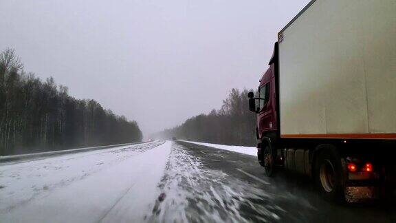 在可怕的多雪多风的天气里重型货车在公路上行驶透过挡风玻璃的视野-驾驶员视角移动视频