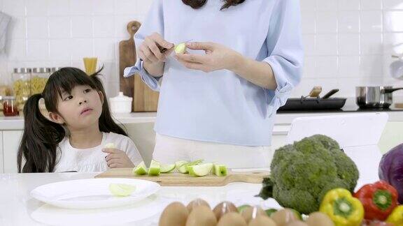 幸福的亚洲家庭妈妈正在准备蔬菜和水果女儿在家里的厨房玩智能手机健康饮食和晨间活动理念