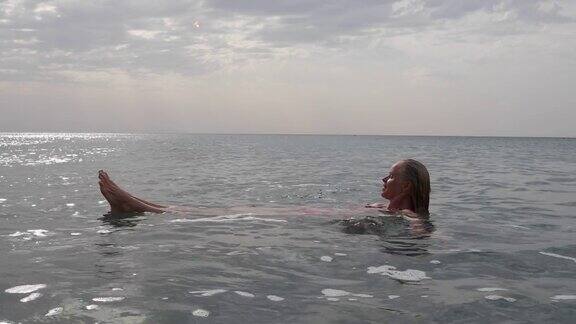 日出时成熟的女人漂浮在平静的海面上