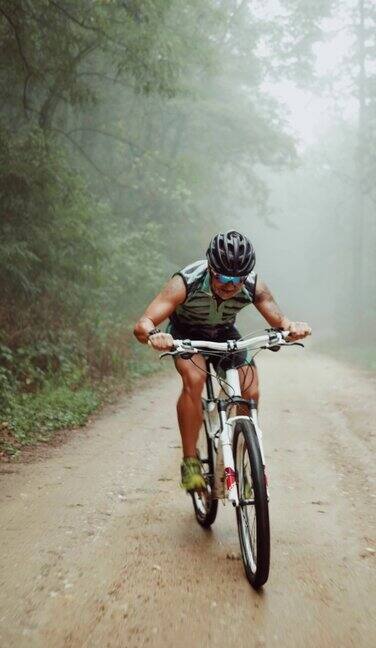 在一个阴天和雨天一个骑自行车的人在森林里爬一条土路的垂直镜头