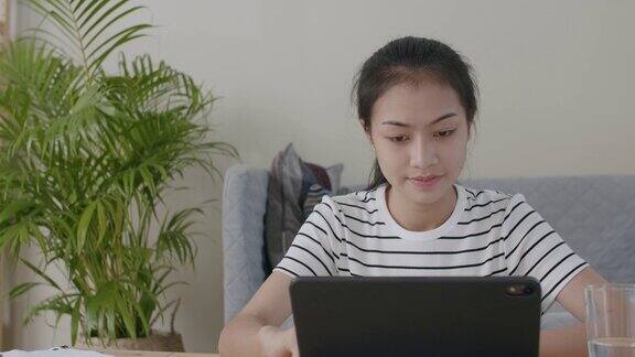 早上一名亚洲妇女坐在客厅里使用笔记本电脑在家在线学习