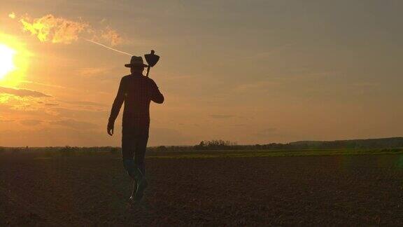 日落时分农民扛着锄头在田园诗般的乡村耕地上