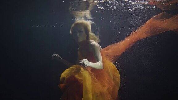 在黑暗的背景下神秘的女人像美人鱼一样在水下游泳