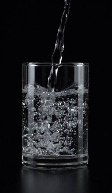 垂直和慢动作:将水倒入一个饮用玻璃在黑色背景