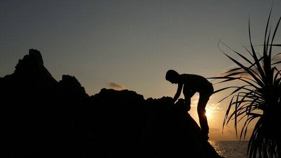 日落时分一个人爬在山上的石头上的剪影