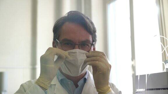 英俊的专业科学家面对镜头微笑然后戴上防护面具
