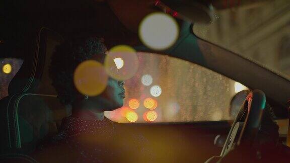 在雨中独自驾车的黑人妇女握着方向盘观察大都市夜晚的道路交通