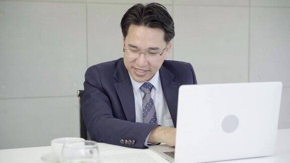 慢动作-亚洲商人在办公室工作与笔记本电脑和文件在他的桌子上顾问律师