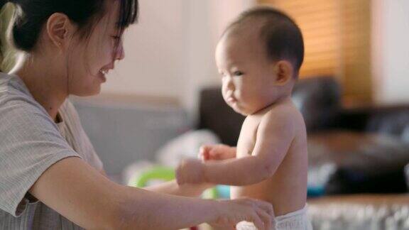 年轻的亚洲妈妈正在给她的宝贝儿子穿衣服(6-11个月)