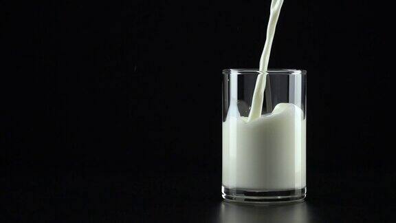 慢动作:将牛奶倒入黑色背景的玻璃杯中
