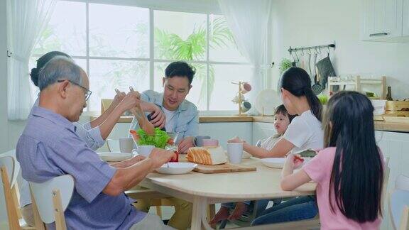 亚洲大家庭在家里的餐桌上一起吃午饭年长的爷爷奶奶、年轻的夫妇和年幼的女儿感到高兴在家里享受吃面包活动关系