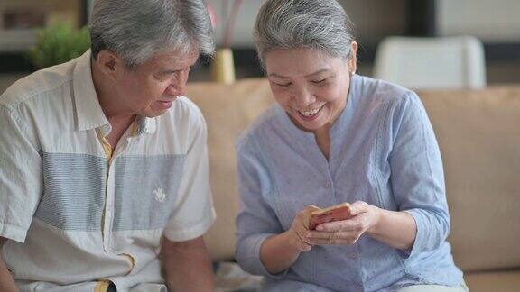 亚洲华人老年夫妇在周末休闲时间在客厅学习使用智能手机