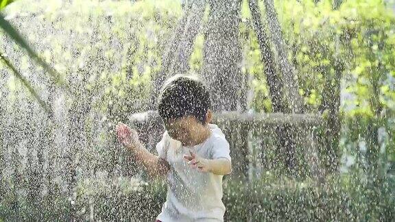 在炎热的夏天小男孩在自家后院的洒水器里玩耍