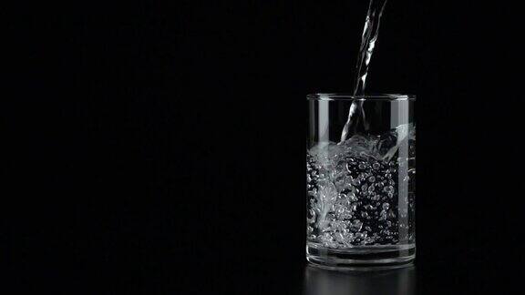 慢动作:在黑色背景下将水倒进玻璃杯