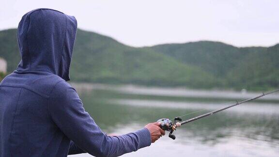 一个渔夫在一个天然的湖边钓鱼背景是山
