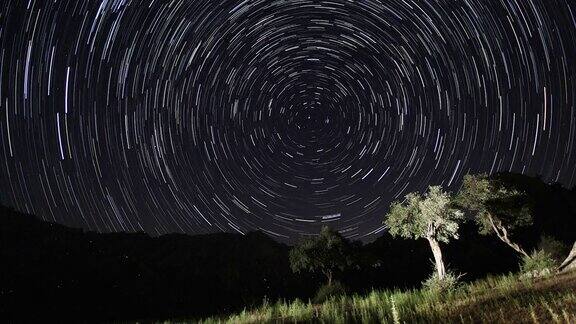 夜空中移动的恒星轨迹的时间间隔在前景中有一座山顶的银河系的星星夜晚天空自然夏季景观英仙座流星雨观测