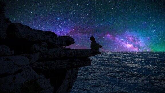 一个男孩的剪影坐在悬崖边看着银河和流星
