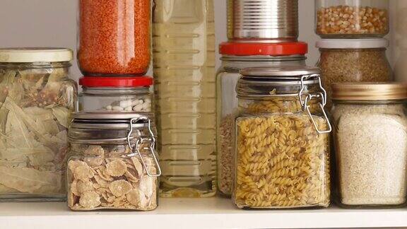 一个男人从食品储藏室的架子上取下或放置装满豆类的玻璃瓶