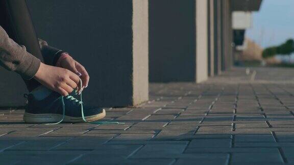 穿着运动鞋的女孩系着鞋带在城市街道上跑步