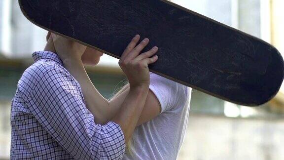 青少年在户外接吻把脸藏在滑板后面害羞的关系