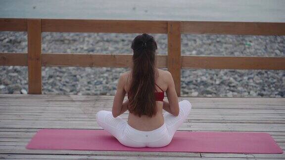 女人坐在莲花的位置和冥想看着海景背部