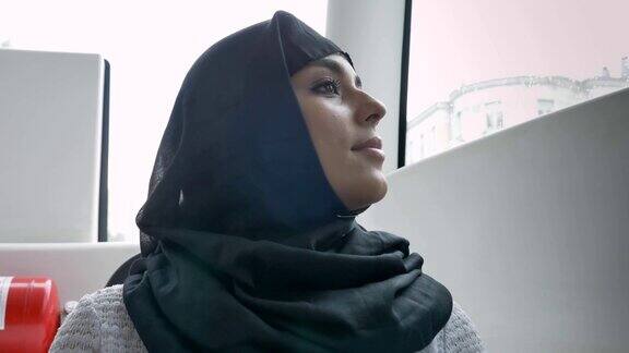 年轻的穆斯林妇女戴着头巾在公交车的窗口观看雨天的天气交通概念城市概念