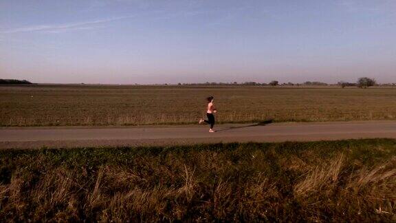 鸟瞰图的年轻女子奔跑在农村道路上的日落