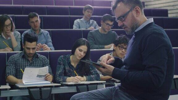一位大学教授正在给一群来自不同民族的学生上课他正在检查一台平板电脑