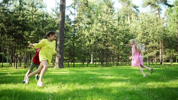 慢镜头拍摄的三个孩子在夏天公园的草坪上玩捉人游戏小朋友们喜欢在阳光明媚的日子里在绿草地上跑步