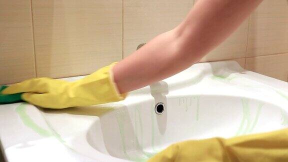 一个戴着黄色橡胶手套的不可辨认的女人正在用绿色海绵清洗浴室的水槽清洁和洗涤概念