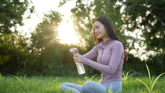 穿着运动服的亚洲女人坐在瑜伽垫上喝水