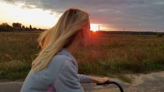 日落时分金发女郎在草地上骑着自行车农村