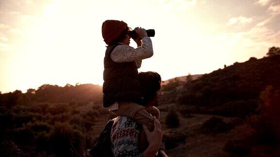 男孩骑在父亲的肩膀上用双筒望远镜看风景