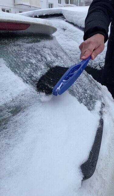 在一个冬天的早晨一名无法辨认的男性司机正在用刷子清理汽车后窗上的新雪
