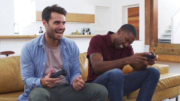两个男性朋友坐在客厅的沙发上玩电子游戏