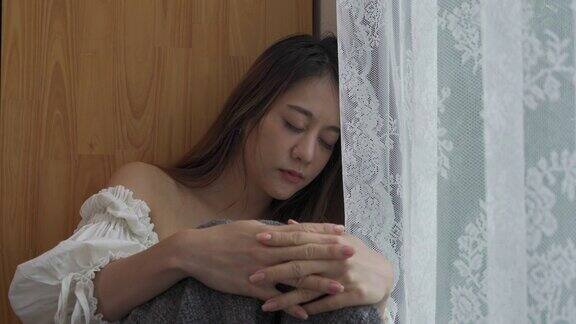 4K沮丧美丽的亚洲女人独自坐在公寓房间的窗户边哭泣和尖叫孤独悲伤的女孩想起悲伤烦恼消极情绪与心理健康