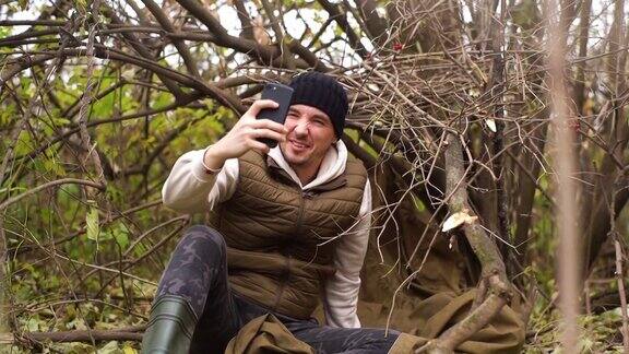 迷路的旅行者男性穿着暖和的衣服坐在森林里试图在阴冷的天气捕捉手机信号
