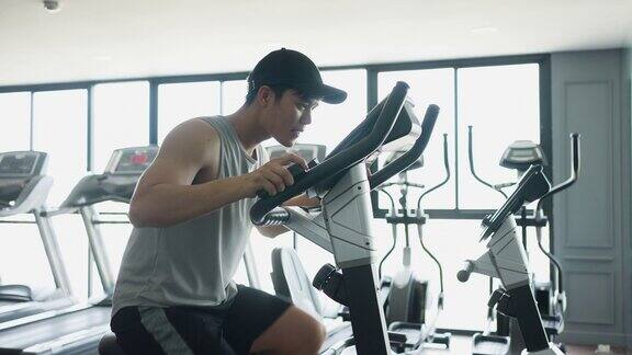 慢动作场景:亚洲青年男子在自行车运动器械上跑步在健身房锻炼和锻炼有氧运动以达到运动训练的生活方式理念