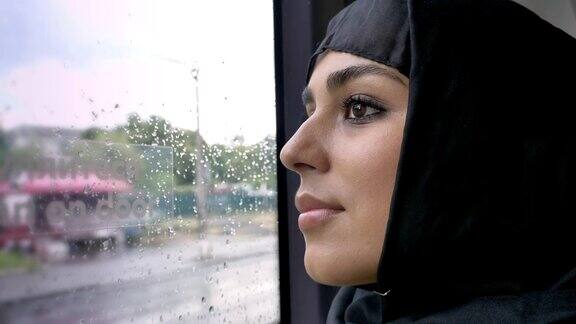 年轻的穆斯林妇女戴着头巾在公共汽车的雨窗中观看交通概念城市概念天气概念梦想概念侧视图