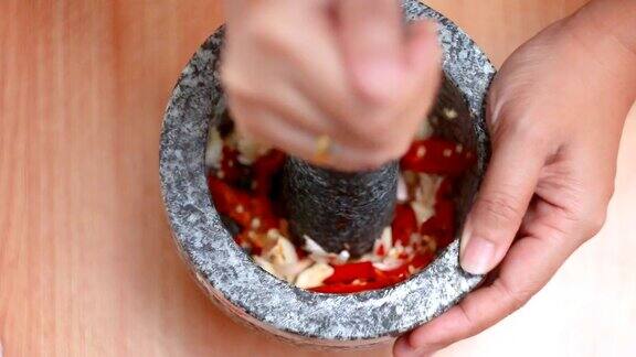 俯视女子用手捶打红辣鲜辣椒和大蒜用臼石准备混合香草调味料烹饪泰国菜前用暖调加工