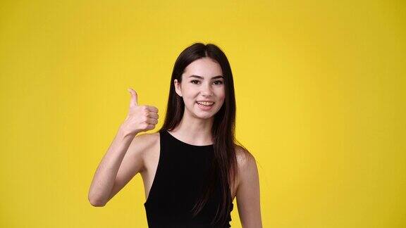 一个女孩在黄色背景下竖起大拇指的4k慢动作视频