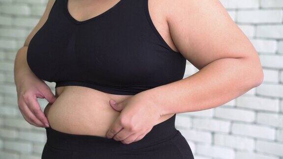 侧视图:泰国超重妇女的手在运动衣服触摸她的肚子感觉无聊