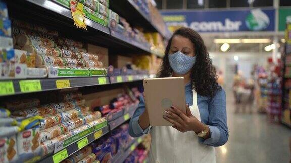 戴着口罩的女人用平板电脑控制超市的库存