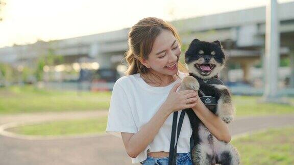 快乐的年轻亚洲女人在公园里玩抱着她的狗宠物情人