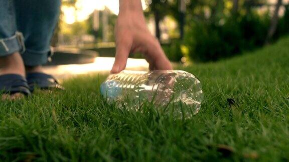 女子手从公园草地上捡起塑料瓶环保理念
