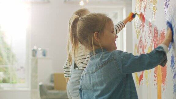两个快乐的小女孩用蘸了彩色颜料的手在墙上画手印他们开心地笑着房屋正在装修