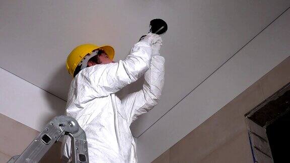 男工人戴着头盔在石膏板天花板上开洞用于照明安装