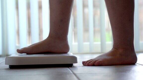 一个光着脚和腿的女人踩在浴室的秤上检查她的体重